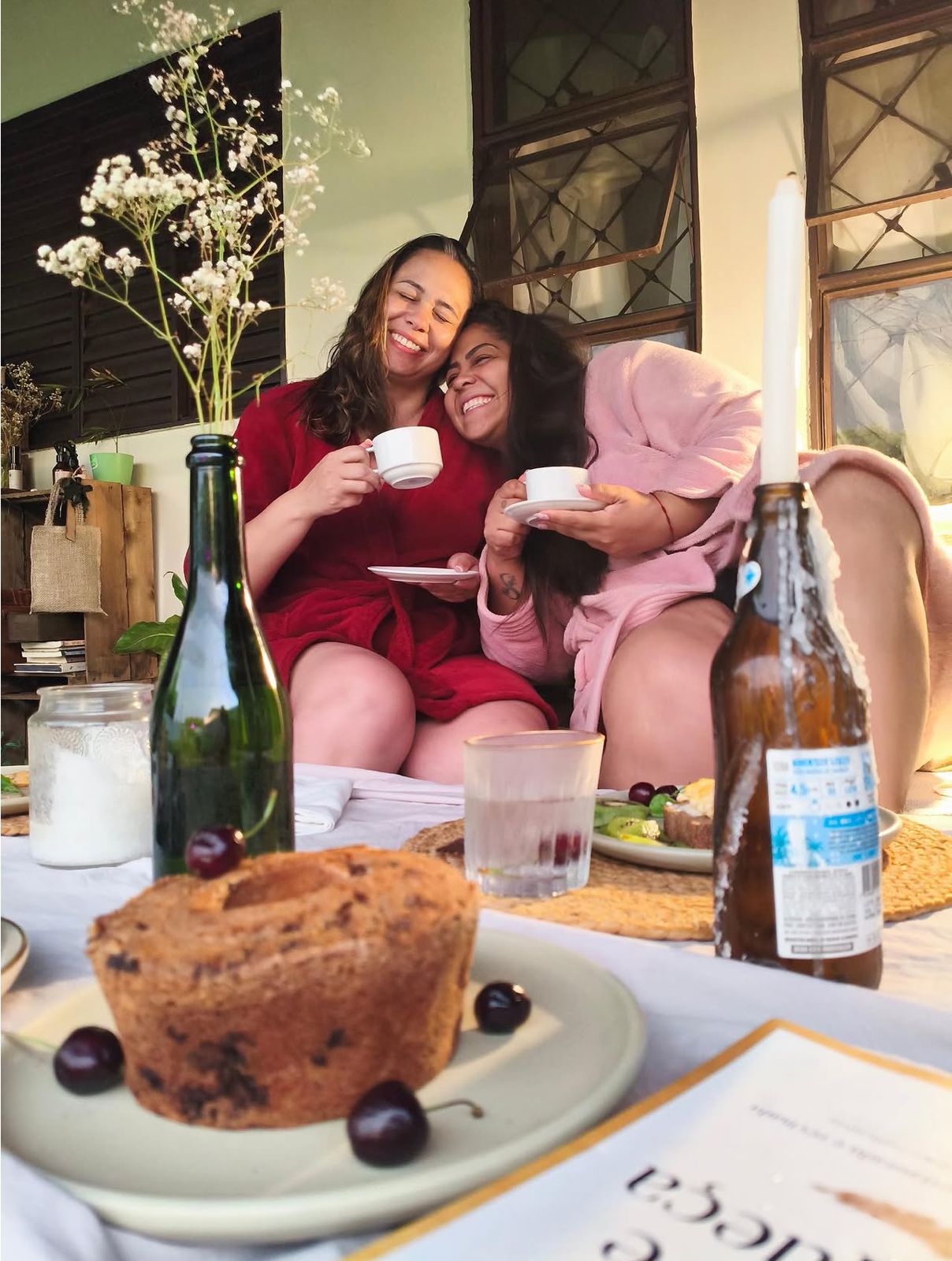 Duas clientes sorrindo com roupões, tomando café na Casa Verde